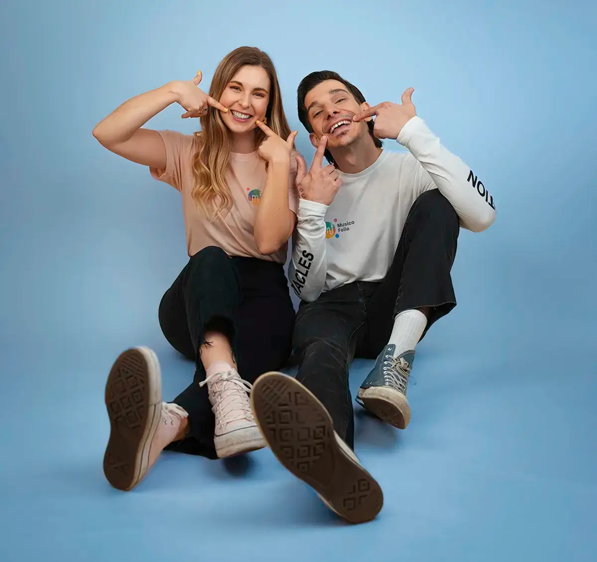 Mariane et Antoine de Musicofolie souriants, assis côte à côte sur fond bleu