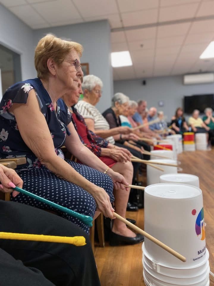 Aînée souriante jouant du tambour lors d'un atelier musical Musicofolie en résidence