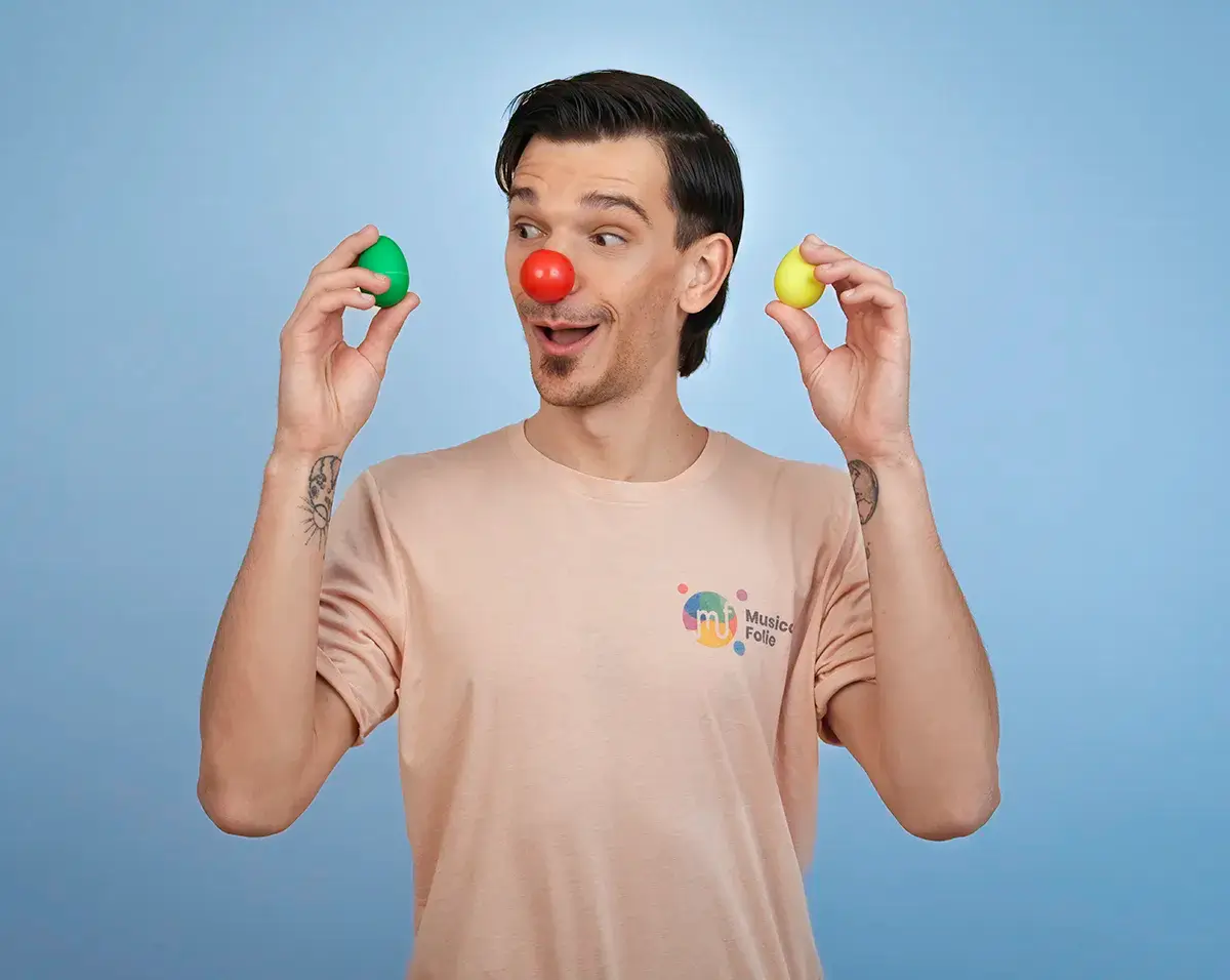 Un animateur de Musicofolie, nez rouge de clown, tenant un œuf shaker vert et un œuf shaker jaune, sur un fond bleu