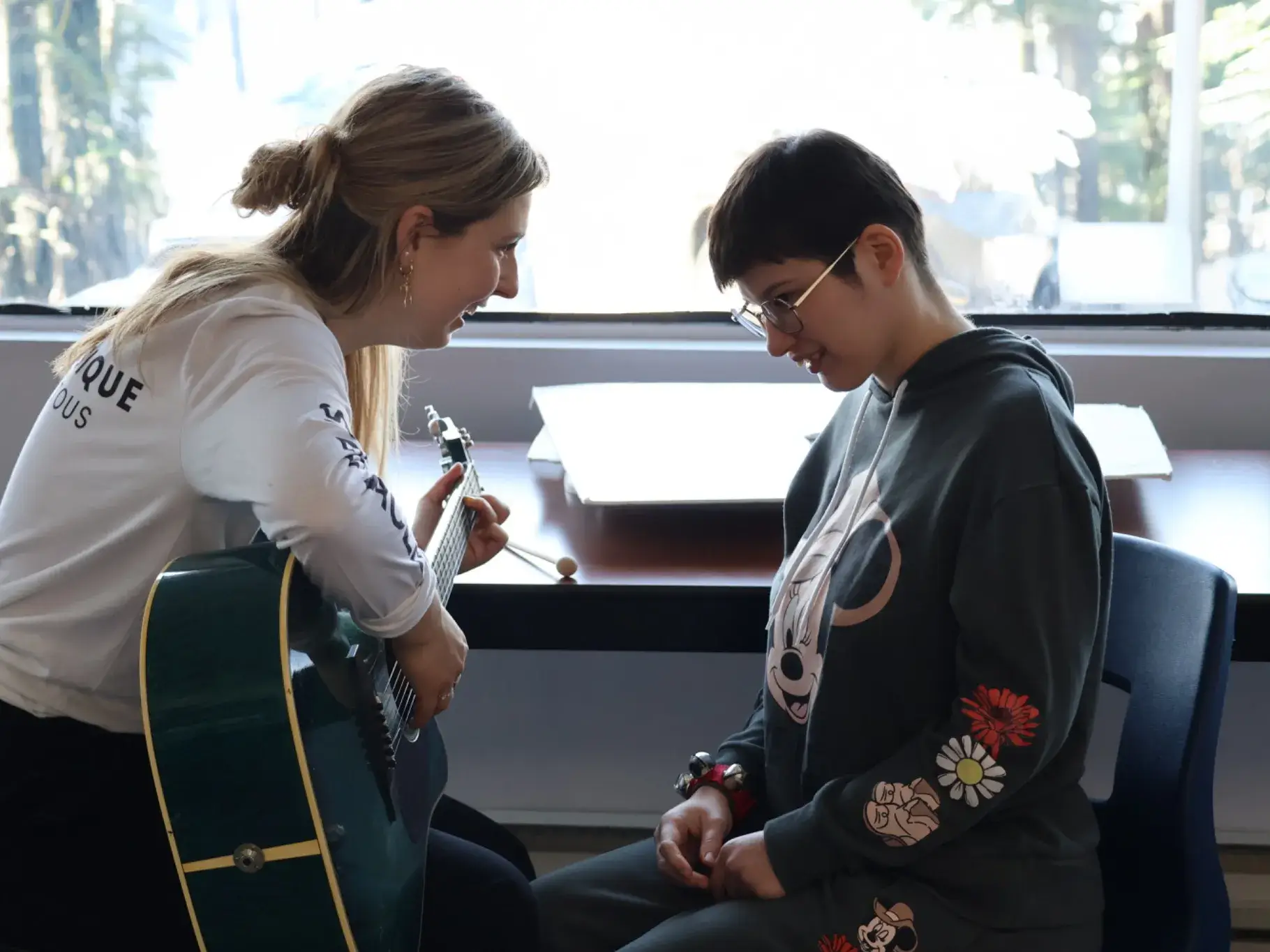 Une animatrice à la guitare sourit à une participante assise près d'une fenêtre
